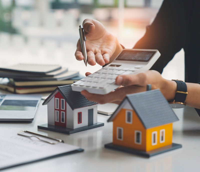 A person calculating costs or mortgage rates with miniature houses on a desk.