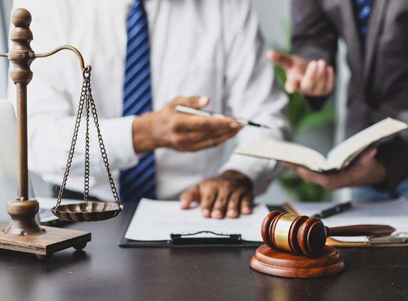 Legal professionals collaborating over paperwork with a gavel and scale in the foreground.