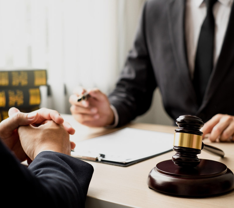 Two people in a legal consultation with a wooden gavel and clipboard on the desk.