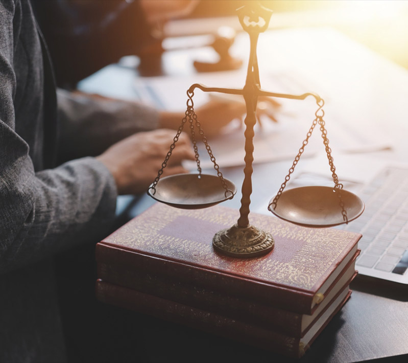Scales of justice resting on law books with a person working in the background.