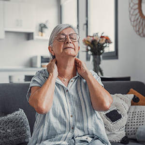 Elderly woman holding her neck in pain, representing personal injury or physical stress.