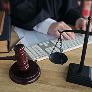 Judge typing on keyboard with gavel and scales of justice on desk; online legal services.