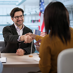 Immigration lawyer shaking hands with client near US flag; citizenship legal services.