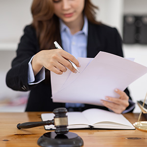 Female attorney holding a pen and reviewing legal documents; professional law firm advice.