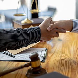 Business partners shaking hands over a contract with a legal gavel; settling legal disputes.