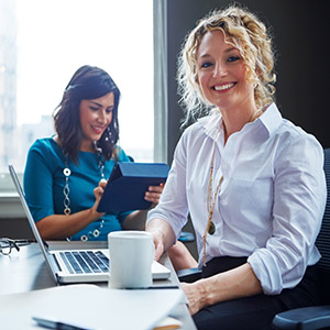 Two smiling legal professionals working together with a laptop and a tablet.