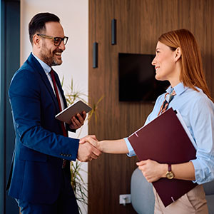 Smiling male lawyer shaking hands with female client in office; professional legal advocacy.