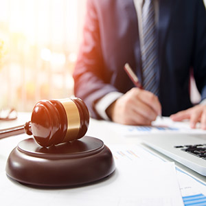 Attorney writing paperwork at office desk with judge gavel featured