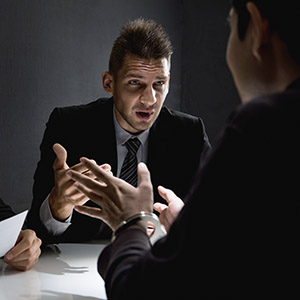 Criminal defense attorney consulting with handcuffed client during interrogation